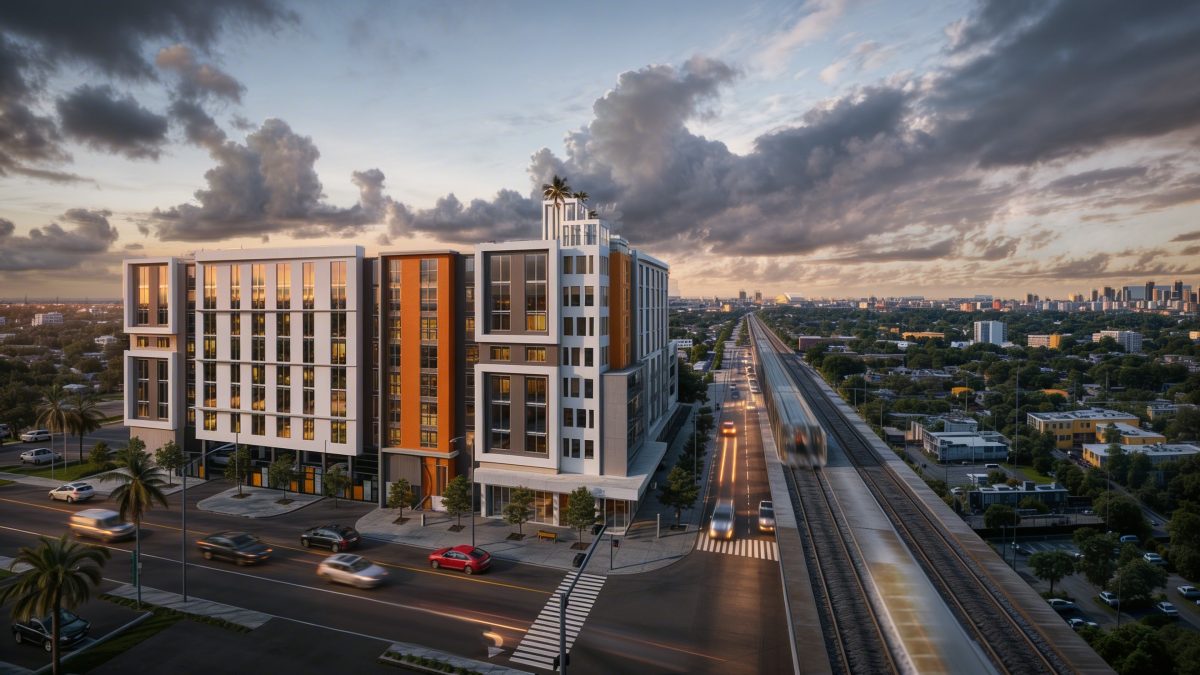 Aerial dusk view of a mid-rise multifamily block beside the rail corridor, the Miami skyline beyond.